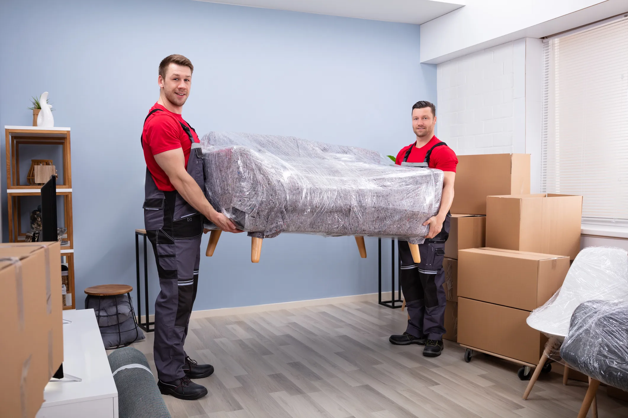 Möbelpacker tragen bei einem Umzug in Wien ein in Stretchfolie verpacktes Sofa durch den Wohnraum